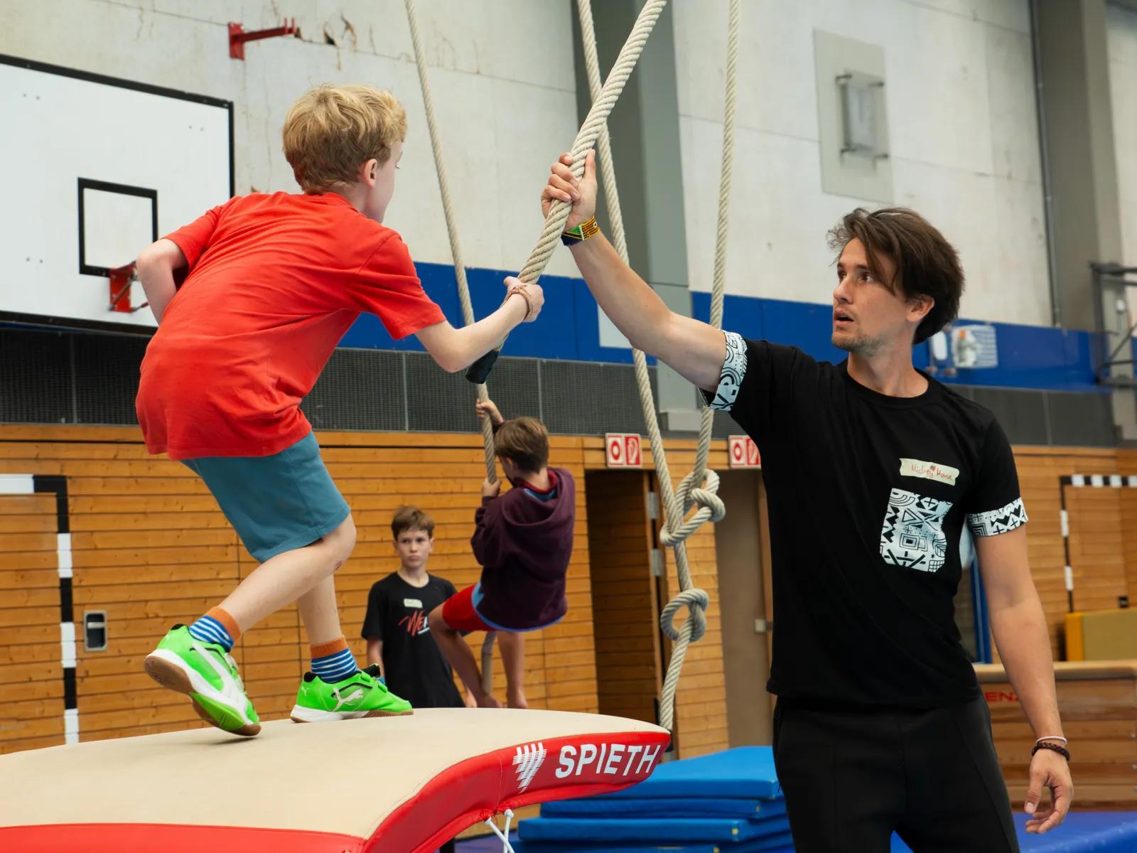 Kind schwingt an einem Seil über eine blaue Matte in der Trainingshalle
