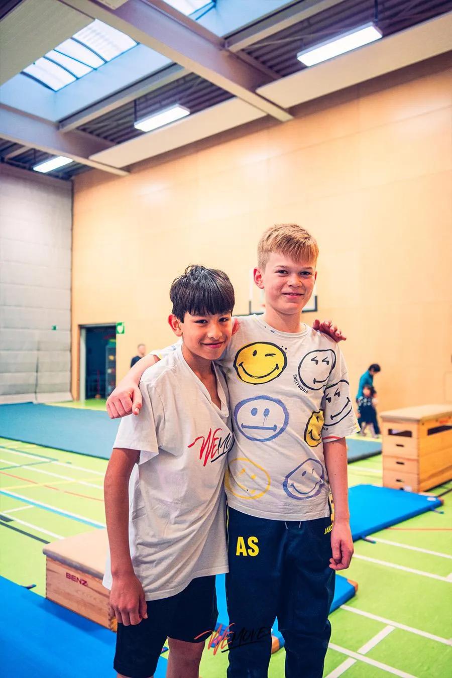 Zwei Jungs stehen lachend Arm in Arm in der Sporthalle
